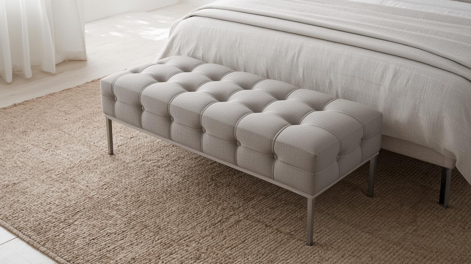Tufted upholstered bench at the foot of a neutral platform bed with a textured rug and natural light.