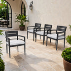 Four black aluminum outdoor dining chairs with white cushions arranged on a stone patio - Elirian