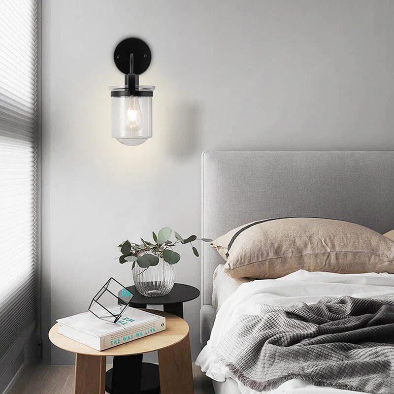 Modern black wall sconce with clear glass shade illuminating minimalist bedroom - Elirian